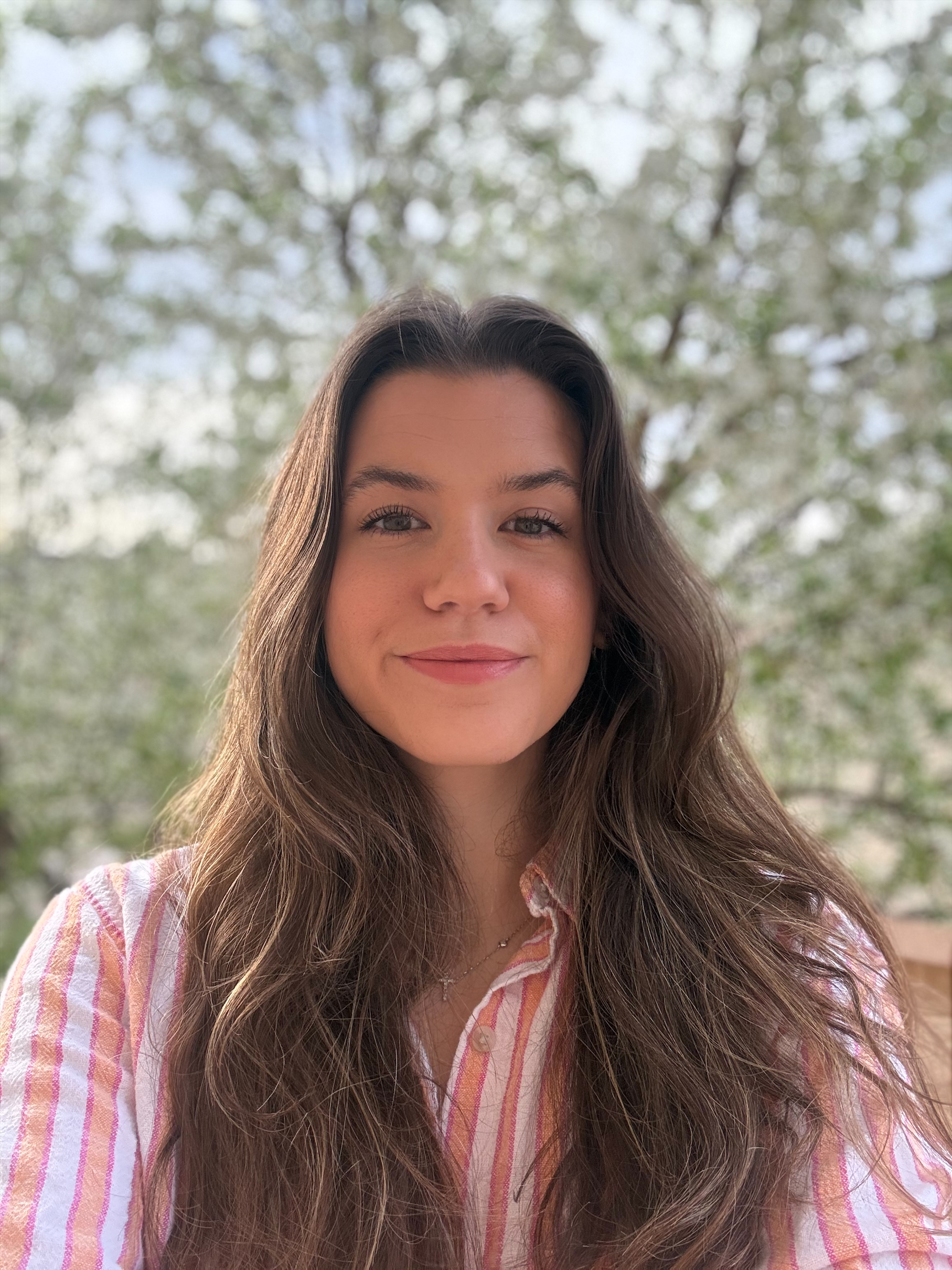 Jenna, a smiling white woman with long brown hair, wearing an orange, pink and white striped shirt. 